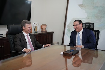 Dos hombres sonrientes, Marco Villeda y Jorgan Andrews, sentados uno frente al otro en una mesa de cristal en una oficina, con un gran mapa de Guatemala de fondo