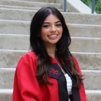 Una mujer joven de cabello negro sonríe vistiendo una túnica de graduación roja sobre unas escaleras de concreto