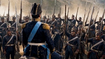 Un oficial militar a caballo, de espaldas, con uniforme azul y dorado, frente a una multitud de soldados en uniforme histórico con fusiles y bayonetas