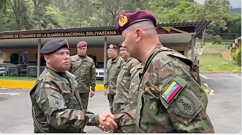 Dos militares de uniforme camuflado y boina se dan la mano. Otros tres militares de uniforme en segundo plano. Edificio con el letrero de la Guardia Nacional Bolivariana