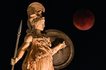 This photograph shows a full moon also known as "Blood Moon" during a lunar eclipse with a statue of ancient Greek goddess Athena in the foreground, in central Athens, on September 7, 2025. (Photo by Angelos TZORTZINIS / AFP)