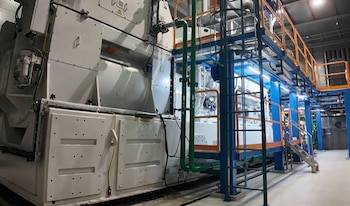 Gran motor industrial gris y blanco con tuberías verdes y plataformas metálicas azules y naranjas en una instalación de procesamiento