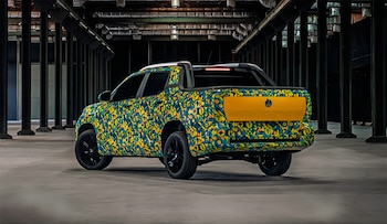 Vista trasera de una pickup Volkswagen Tukan con camuflaje de patrón amarillo, azul y verde, estacionada en un espacio interior oscuro con columnas