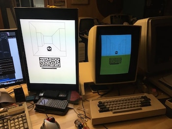 Dos monitores de computadora, dos teclados, un ratón trackball, un dispositivo PDA y cables sobre un escritorio de madera