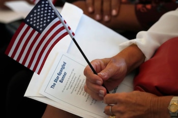 Primer plano de manos de una persona sosteniendo una pequeña bandera de Estados Unidos y un folleto que muestra el título "The Star-Spangled Banner"