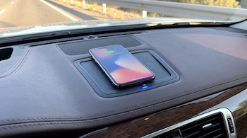 Teléfono móvil cargando de forma inalámbrica sobre el salpicadero de un coche, con la carretera visible a través del parabrisas.