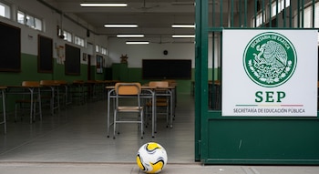 Balón de fútbol en entrada de escuela pública mexicana vacía. Cartel de la SEP en reja. Aulas con pupitres ordenados al fondo.