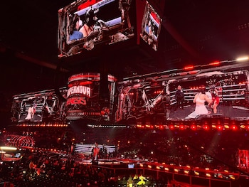 Uma arena com luzes vermelhas, dois lutadores em um ringue de boxe, um árbitro e uma tela gigante de LED mostrando a ação e o logotipo ‘Supernova Genesis’