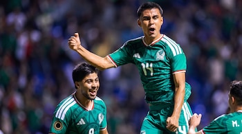 Tres jugadores de fútbol con uniformes verdes y blancos de la selección de México. Uno levanta el pulgar, otro sonríe, el tercero se ve de espalda.