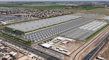 Render aéreo de un gran complejo de centro de datos con edificios y contenedores blancos, adyacente a viviendas, campos verdes y una carretera con coches