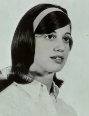 Retrato en blanco y negro de una mujer joven con cabello oscuro peinado, diadema clara, y camisa blanca, sobre un fondo liso