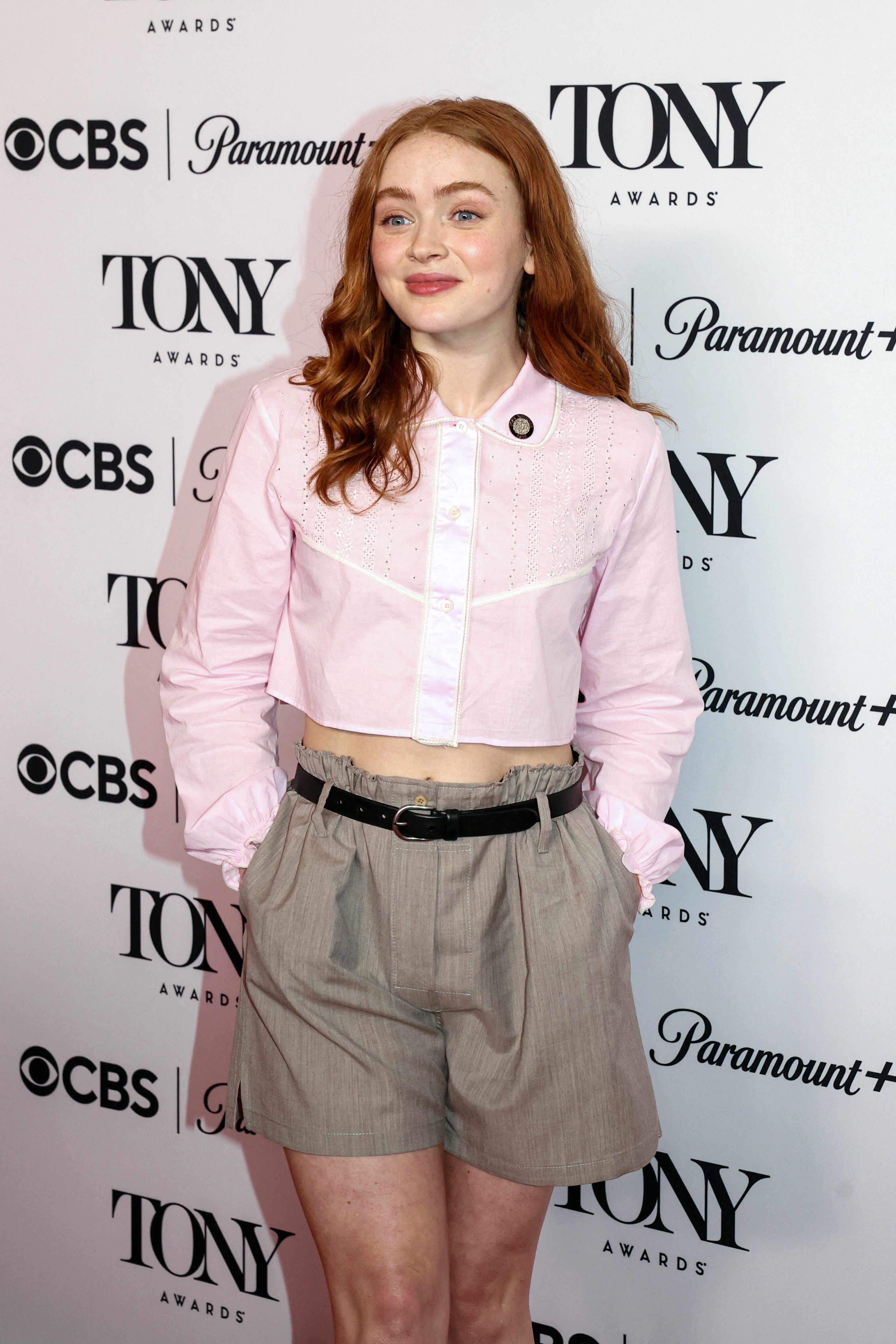 Sadie Sink durante su paso por los Premios Tony, con bermuda beige de tiro alto, camisa rosa claro y cinturón negro fino (REUTERS)