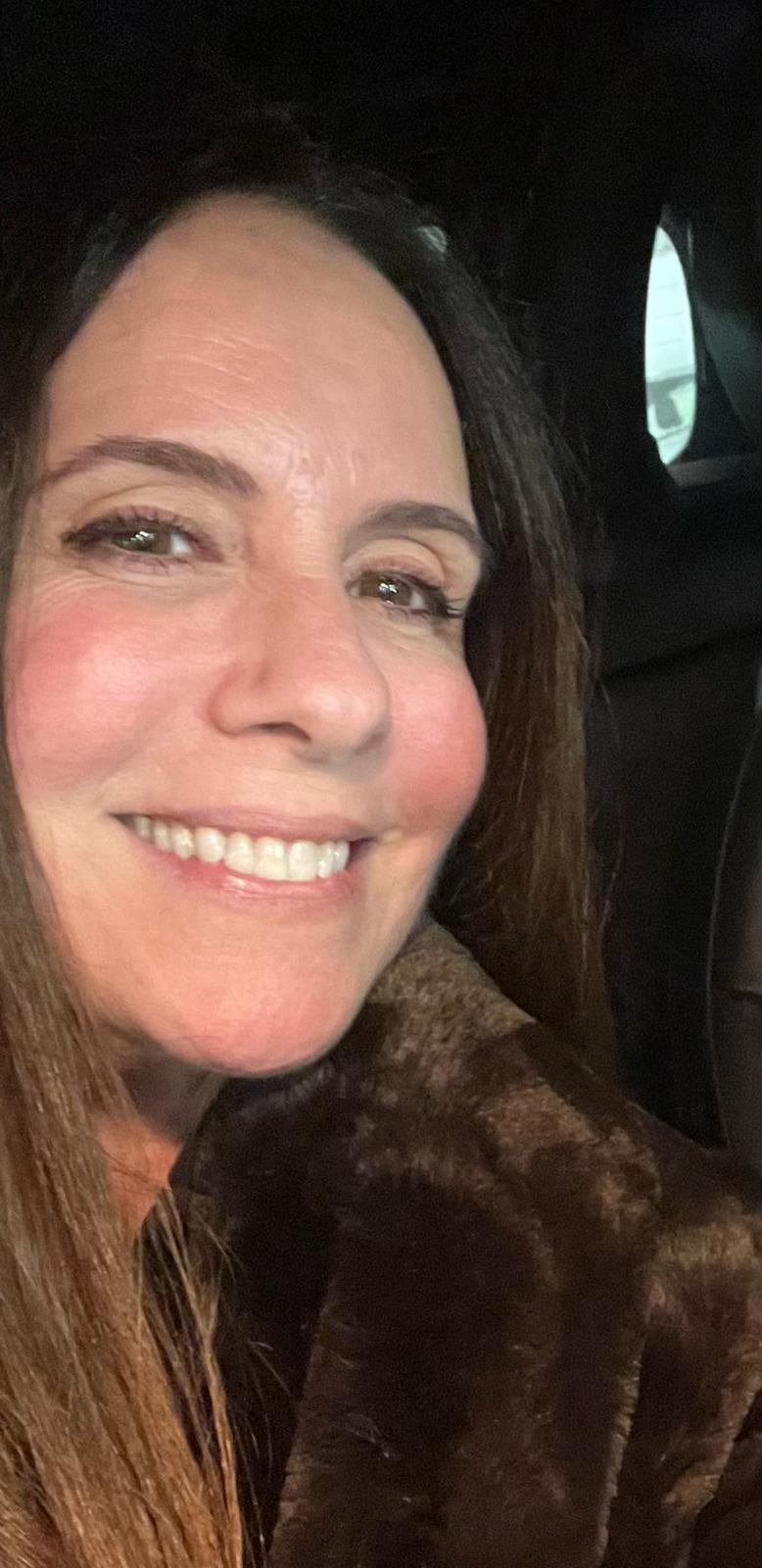 Noelle Balfour sonríe a la cámara mientras viste un abrigo de color marrón en el interior de un vehículo.