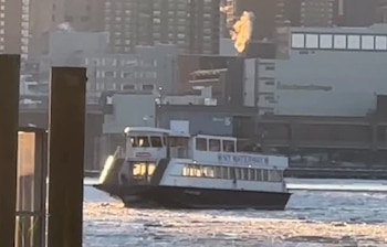 Ferry blanco y negro 'NYC Waterway M' navega en agua con hielo. Edificios urbanos de fondo. Pilar oscuro en primer plano izquierdo