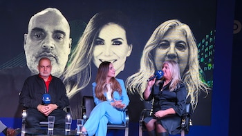 Tres panelistas, un hombre y dos mujeres, sentados en sillas negras sobre un escenario. Detrás, una gran pantalla muestra tres retratos faciales. La mujer a la derecha habla por micrófono de Ticmas