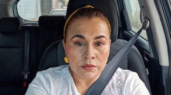 Pintura al óleo de una mujer con blusa blanca, vincha amarilla y cinturón de seguridad dentro de un vehículo.