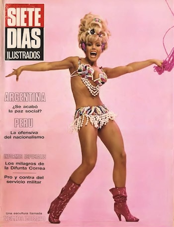 Nelida Lobato, con cabello rubio voluminoso, bikini decorado y botas rojas, posa con brazos abiertos y boca abierta sobre un fondo rosa