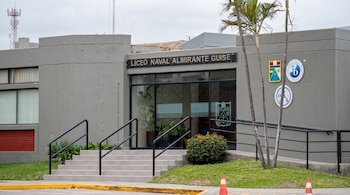 Entrada de un edificio gris con el letrero Liceo Naval Almirante Guise, escalones de concreto, barandas negras y palmeras al frente.