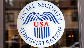 Primer plano del logo blanco de la Administración del Seguro Social en una ventana, con el águila azul y texto 'USA' rojo, reflejos del exterior