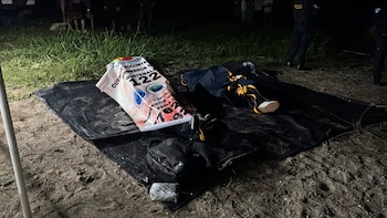 Varias personas, rescatistas con chalecos anaranjados y un agente policial junto a una lancha blanca llamada Kej en una orilla nocturna