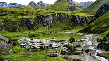 Un poblado con casas pequeñas se ubica en un valle verde rodeado de montañas rocosas y atravesado por un río