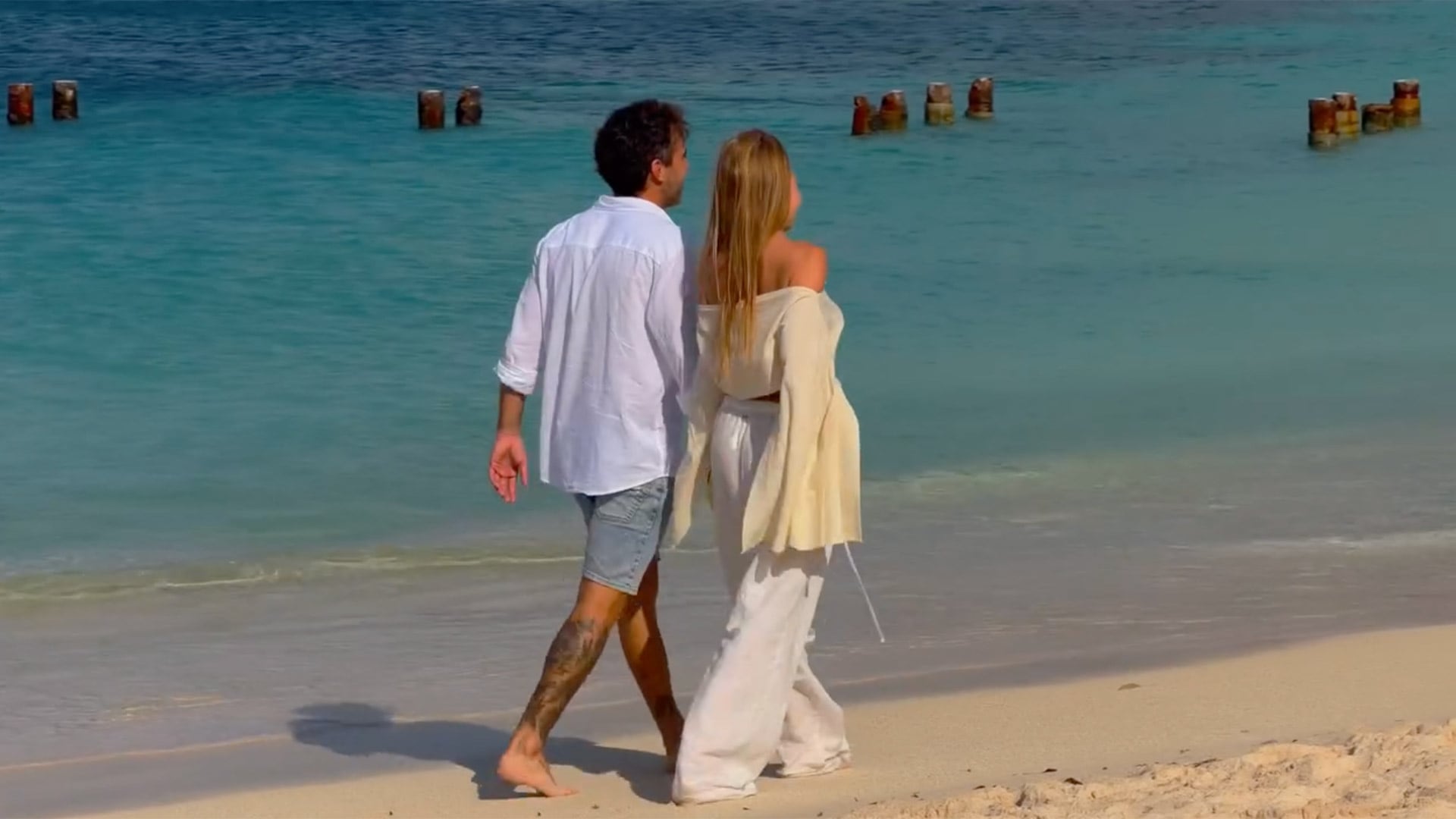 Una caminata en la orilla: la pareja disfruta de la playa y el atardecer, con los pies en la arena y el mar cristalino como testigo de su luna de miel