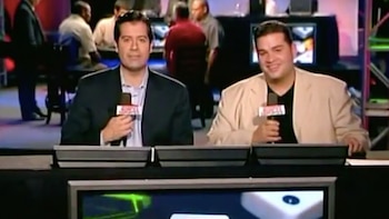 Dos hombres con saco y camisa sostienen micrófonos sentados tras un escritorio con el logotipo de ESPN Deportes