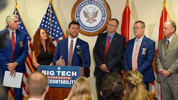 Un hombre habla en un podio con el mensaje Big Tech ante funcionarios y banderas de Estados Unidos y Florida