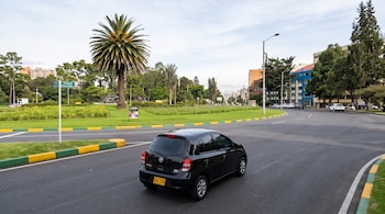 Un automóvil negro avanza por una vía asfaltada curva con árboles, una palmera y una señal que dice Parque Nacional.