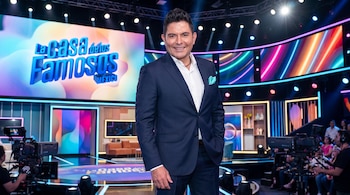 Ernesto Laguardia sonríe de cuerpo completo, viste traje oscuro, camisa blanca y pañuelo claro, en estudio con cámaras, pantallas y el logo 'La Casa de los Famosos México'.