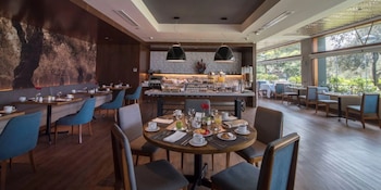 Interior de El Olivar Restaurante con un buffet de desayuno, mesas redondas y rectangulares con sillas, y ventanales con vista a un jardín