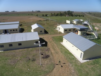 Varios edificios de planta baja con techos de chapa gris y paredes claras se ubican en un predio rural con cercado y postes de luz