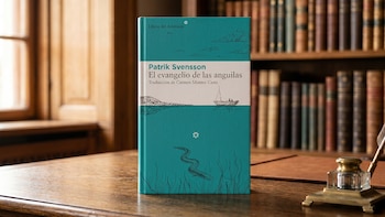 Un libro de tapa blanda azul verdoso, 'El evangelio de las anguilas', de Patrik Svensson, se alza verticalmente sobre un escritorio de madera pulida. Al fondo, una ventana y una estantería
