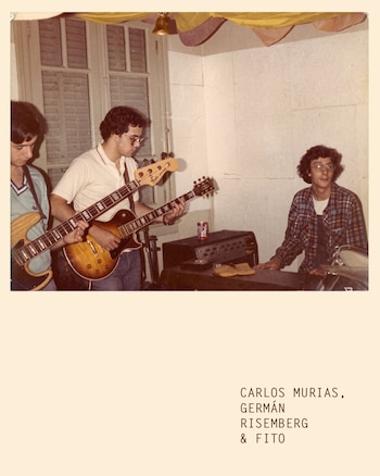 Tres jóvenes músicos en un interior, dos con guitarras eléctricas y uno sentado frente a un teclado, con una ventana al fondo