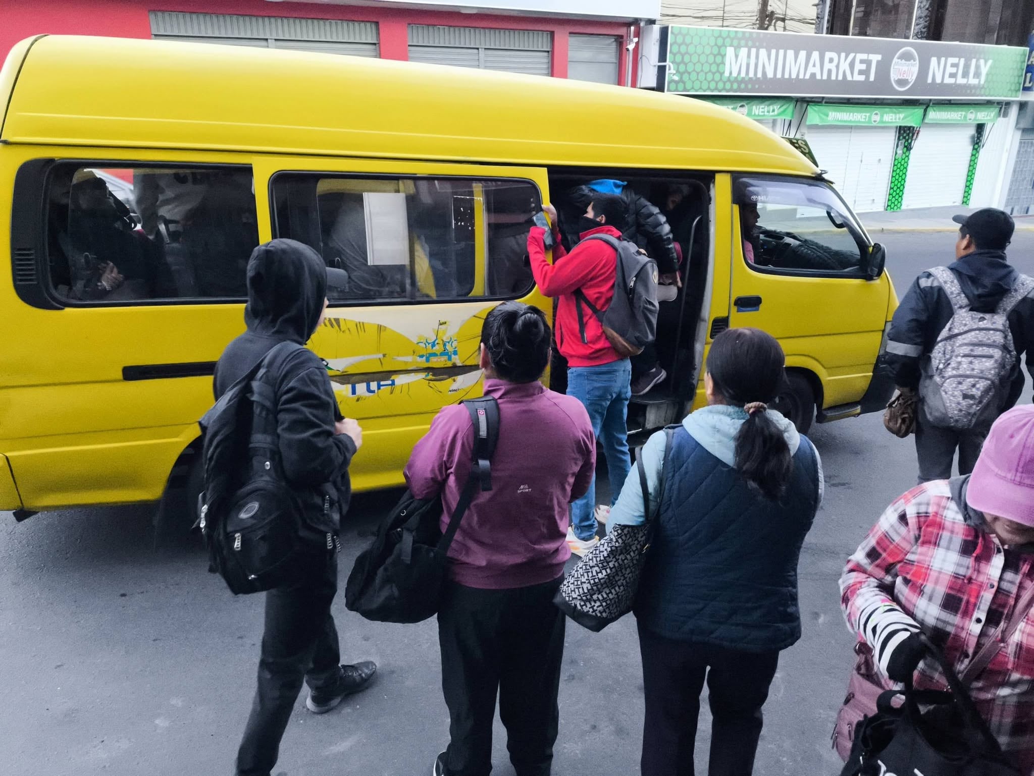Personas intentan abordar una van amarilla en Arequipa, Perú, en medio de un paro de transportistas que ha afectado el servicio de transporte público. (La Vanguardia)