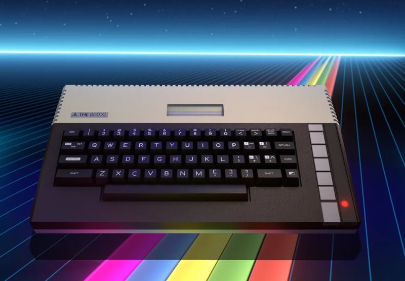Una computadora Atari 800XL reposa sobre una cuadrícula digital con franjas luminosas de colores y un fondo de estrellas. (Foto: Atari)
