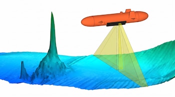 Un vehículo submarino autónomo naranja con equipo de sonar negro proyecta haces de luz amarilla sobre un fondo marino con relieves azules y verdes.