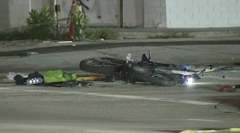 Una motocicleta tendida sobre el asfalto junto a una mochila verde y escombros dispersos en una calle nocturna