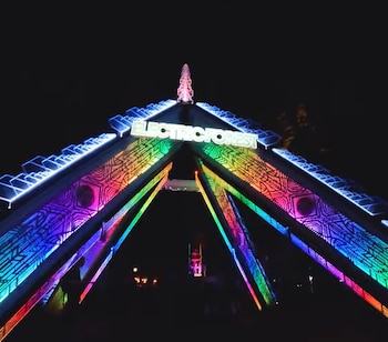 Estructura triangular iluminada con el texto Electric Forest en la parte superior, mostrando colores de arcoíris sobre un fondo de cielo nocturno