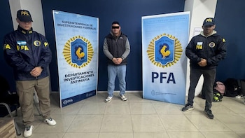 Hombre con rostro difuminado de pie entre dos agentes de la Policía Federal Argentina, frente a banners azules con logotipos de la PFA y textos institucionales