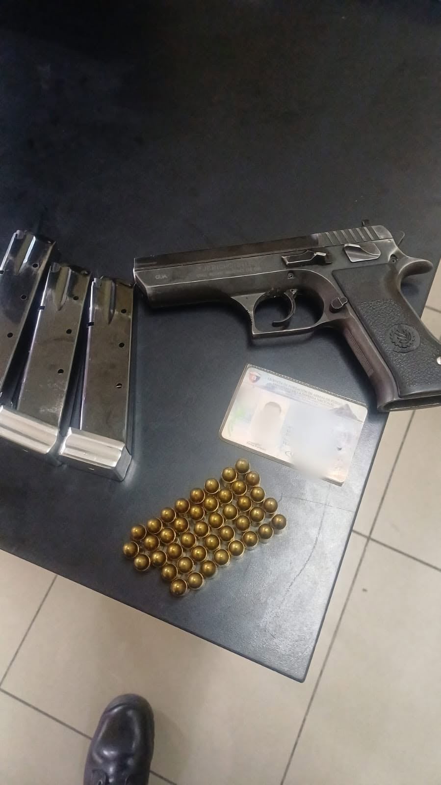 Una pistola tipo Jericho, tres cargadores, decenas de municiones y una tarjeta de portación de armas permanecen alineados sobre una mesa. (PNCdeGuatemala)