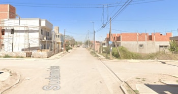 Vista de una calle de tierra en una zona residencial, con casas a medio construir y postes de luz bajo un cielo despejado. El nombre "Sudamérica" es visible en la calle