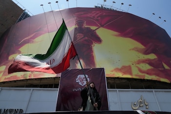 Una mujer ondea la bandera iraní junto a una valla con la imagen del ayatolá Alí Khamenei, muerto el 28 de febrero, mientras Teherán condiciona la reapertura de Ormuz a que EEUU "corrija su comportamiento" (AP Foto/Vahid Salemi)