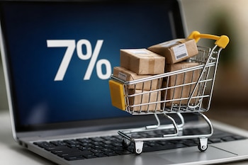 Un carrito de compras miniatura con pequeñas cajas de cartón sobre el teclado de una computadora portátil que muestra el texto 7% en pantalla.