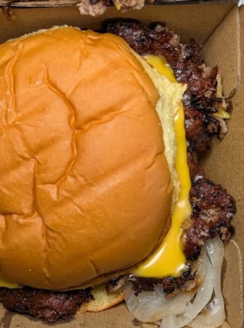 Oklahoma-style smash de res alimentada con pasto, cebolla caramelizada y queso americano en pan Martin’s Potato Roll