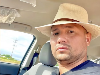 Primer plano de Oswaldo José Cheremo Carrasquel, un hombre con sombrero de paja y barba, sentado en el asiento del pasajero de un coche