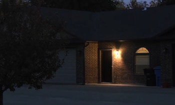 Fachada de ladrillo de una casa de noche con una luz exterior encendida junto a una puerta abierta y un garaje cerrado