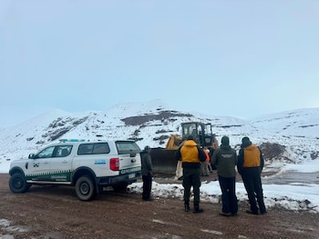Camioneta de Gendarmería Nacional, varias personas, un bulldozer amarillo, camino de tierra, nieve y montañas nevadas bajo un cielo nublado