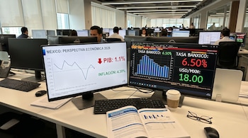 En una oficina moderna, dos monitores muestran gráficos de la economía mexicana con datos de PIB, inflación y tasa de Banxico, junto a un informe financiero abierto.