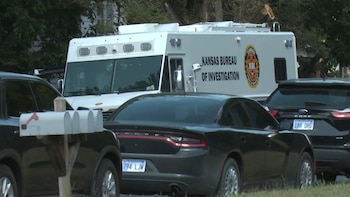Camioneta blanca con logo KBI, un sedán negro, un SUV oscuro, buzones de correo blancos en un poste de madera